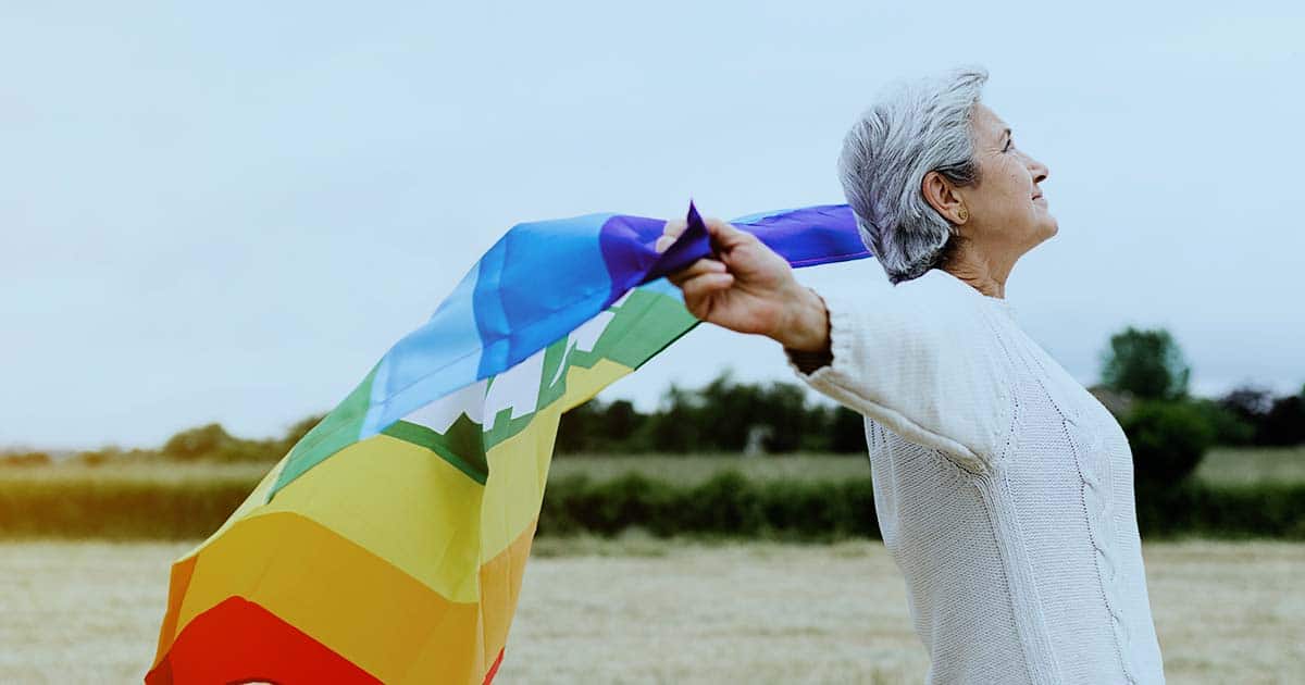 Senior lady holds lgbt flag in field